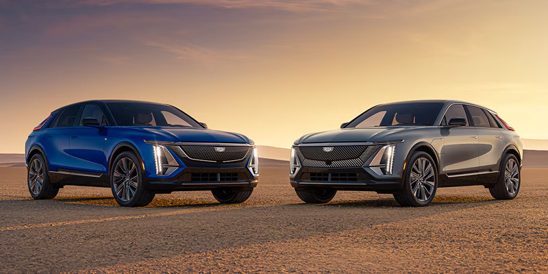 Two Cadillac Lyriq electric SUVs parked in a desert setting during sunset.